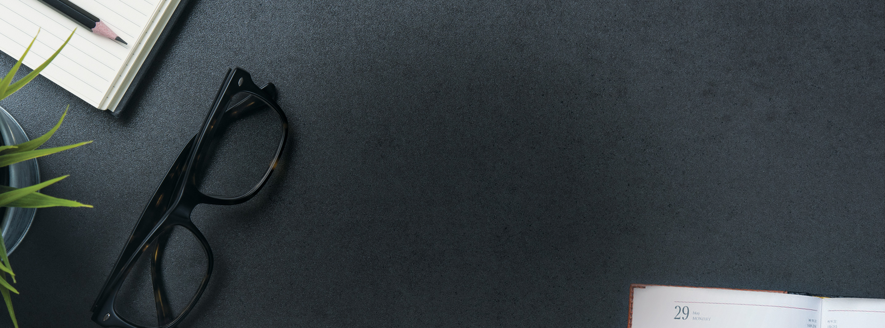 Black pair of glasses laying on desk with notebook and calendar.